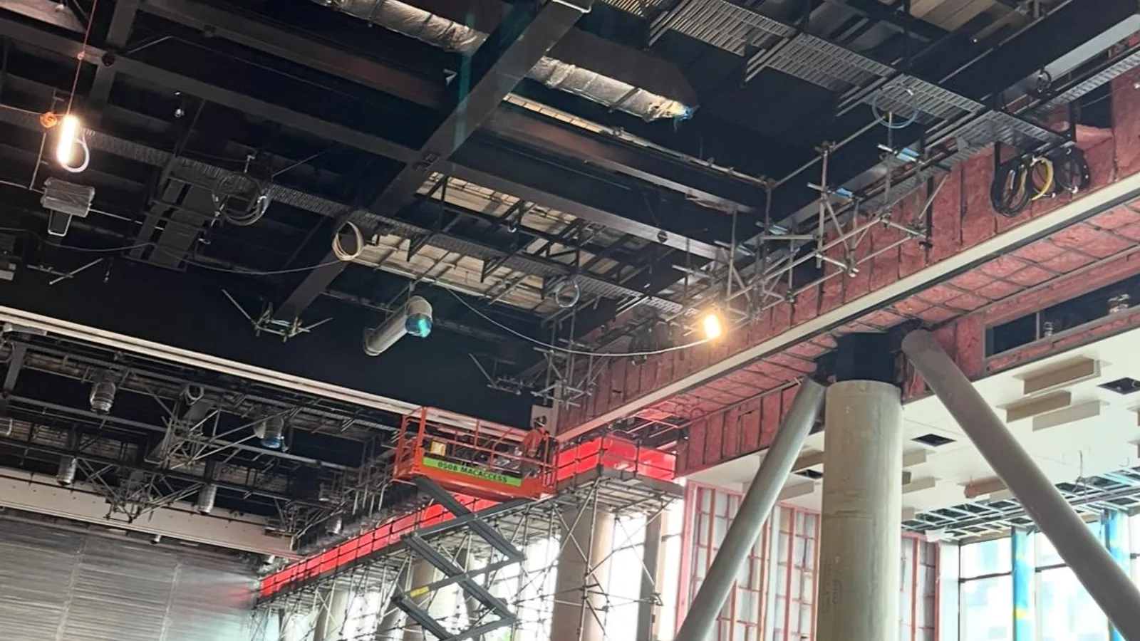 R-Value crew installing acoustic and thermal systems from a scissor lift on a tier-one Auckland commercial fitout: HVAC ducting and structural steel above, scaffolding deck mid-frame.